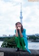 A woman in a blue shirt and green pants sitting on a wall.