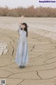 A woman in a blue dress standing in the middle of a desert.