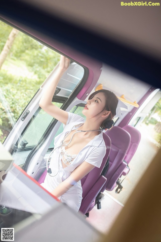 A woman in a white dress is sitting in a bus.