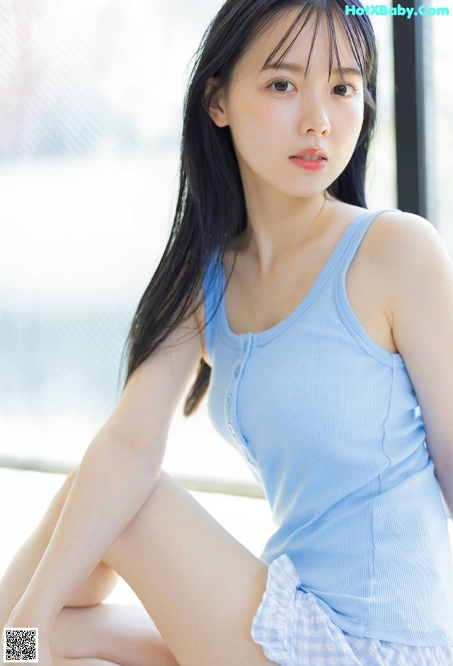 A woman in a blue tank top sitting on a window sill.