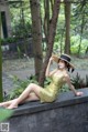 A woman in a yellow dress and straw hat sitting on a wall.