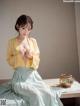 A woman in a yellow blouse and green skirt sitting on a table.