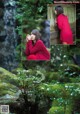 A woman in a red dress sitting on a bench in front of a waterfall.