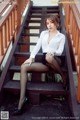 A woman in a white shirt and black skirt sitting on some stairs.