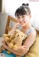 A young girl sitting on a bed holding two teddy bears.